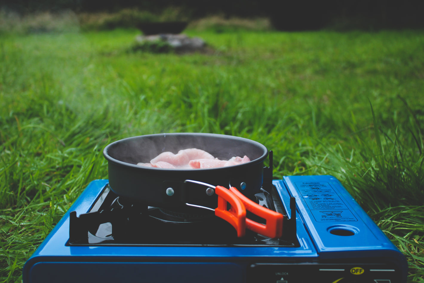 A horizontal camping gas stove cooking a camping pan full of food.